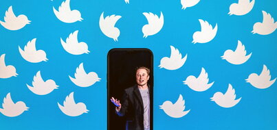 vMontaje en el que aparece una fotografía de Elon Musk en un smartphone que está situado delante de una pantalla de ordenador con el fondo lleno de los característicos logos de Twitter.