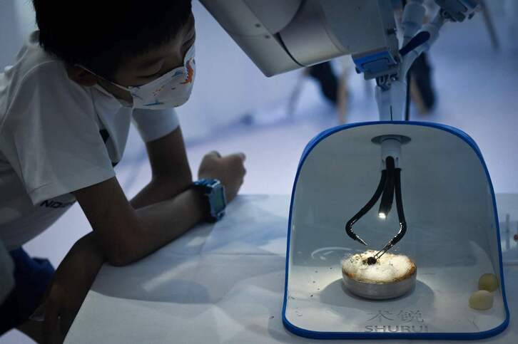 Un niño mira cómo un brazo robótico para cirugía pela la cáscara de un huevo de codorniz en la Conferencia Mundial de Robots 2022 de Pekín.