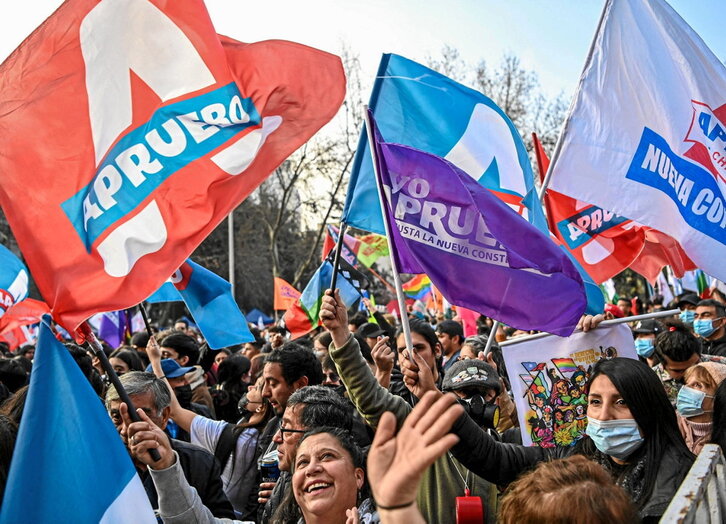 Una persona sostiene varios ejemplares de la nueva Constitución con el palacio de la Moneda como telón de fondo.