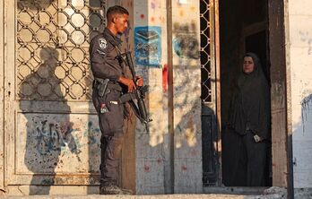 Uma mujer palestina observa a un soldado israelí desde la puerta de su casa