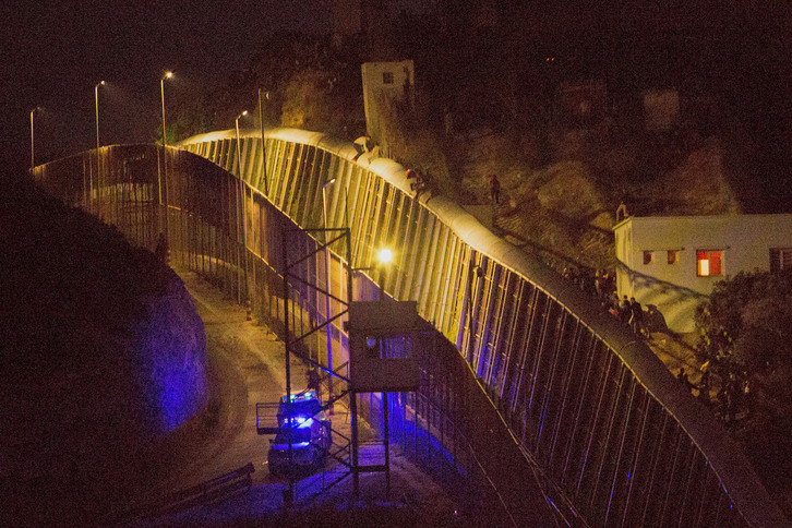 Varias personas tratando de saltar la valla de Melilla mientras policías les aguardan al otro lado, en una imagen de archivo. 