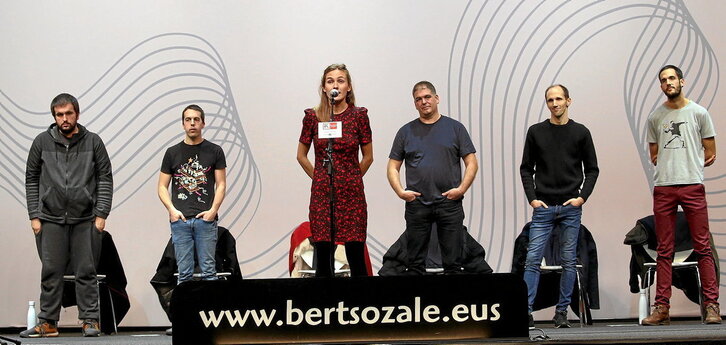 Aurreko orrialdean, Nerea Ibarzabal mikroaren aurrean, gainontzeko bertsolariak begira dituela. Lerron gainean, Sustrai Colinak Ibarzabal zoriontzen.