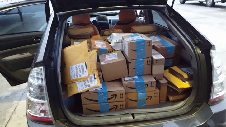 El maletero de un vehículo, a rebosar de paquetes de Amazon.  