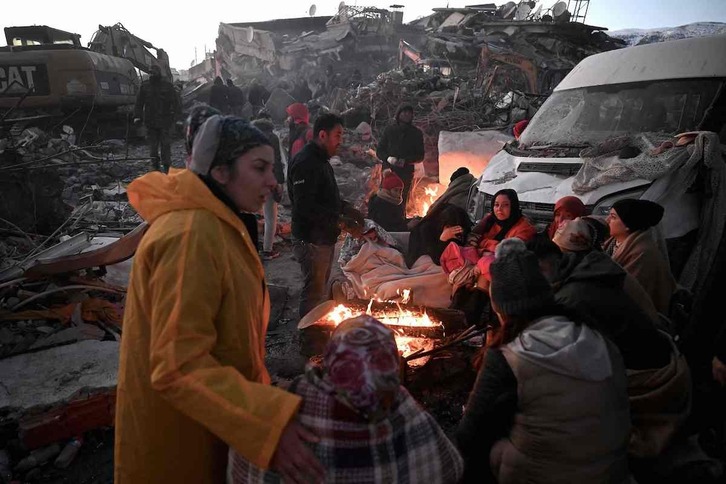 Las personas se paran cerca de una hoguera en medio de los escombros de los edificios derrumbados en Kahramanmaras.