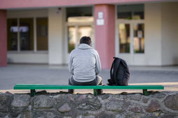 Un joven sentado solo frente a un centro educativo.