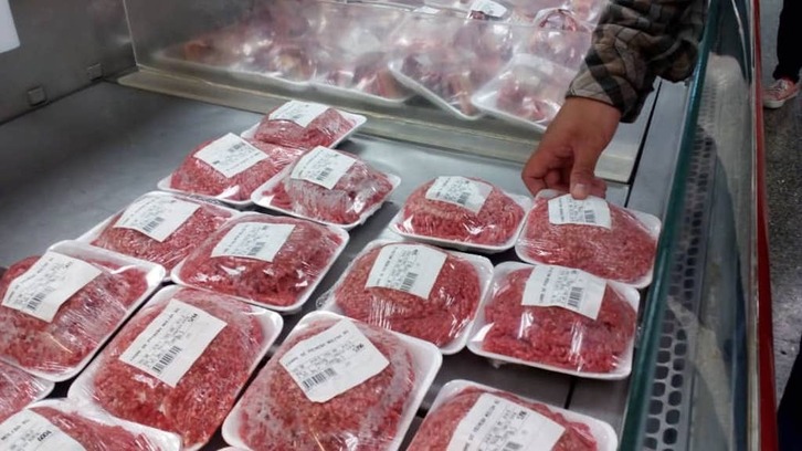 Una persona elige un producto cárnico envasado en un supermercado.