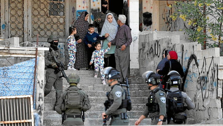 Familia palestinar bat, bere etxearen aurrean, soldadu israeldarrak miaketa egiten ari diren bitartean.