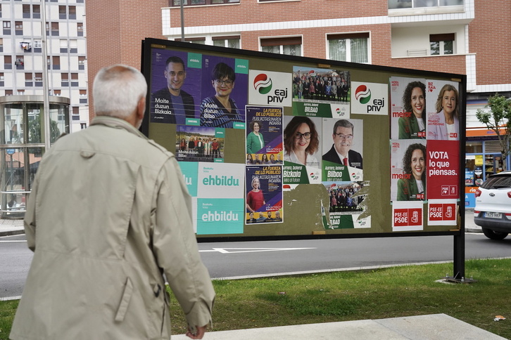 Hautagaien afixez beteriko hauteskunde panel baten aurrean pasatzen ari da gizon bat Bilbon.