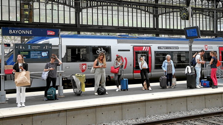 En tren regional o TER, en la estación de Baiona, en uno de cuyos andenes varios pasajeros esperan para emprender viaje.