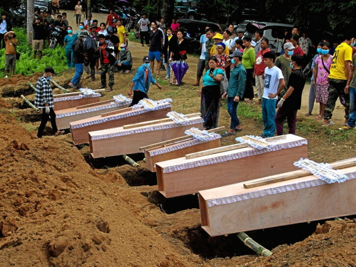 Varios ataúdes, junto a las tumbas, en un funeral conjunto.