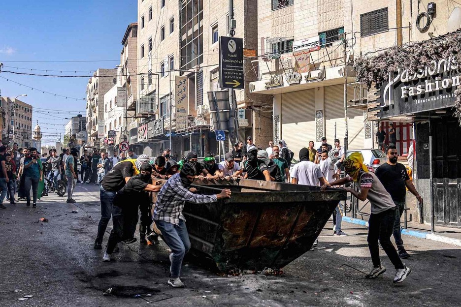 Manifestantes palestinos empujan un contenedor de basura para cubrirse durante los enfrentamientos con las fuerzas israelíes tras una concentración en solidaridad con Gaza en Hebrón. Manifestantes palestinos empujan un contenedor de basura para cubrirse durante los enfrentamientos con las fuerzas israelíes tras una concentración en solidaridad con Gaza en Hebrón.