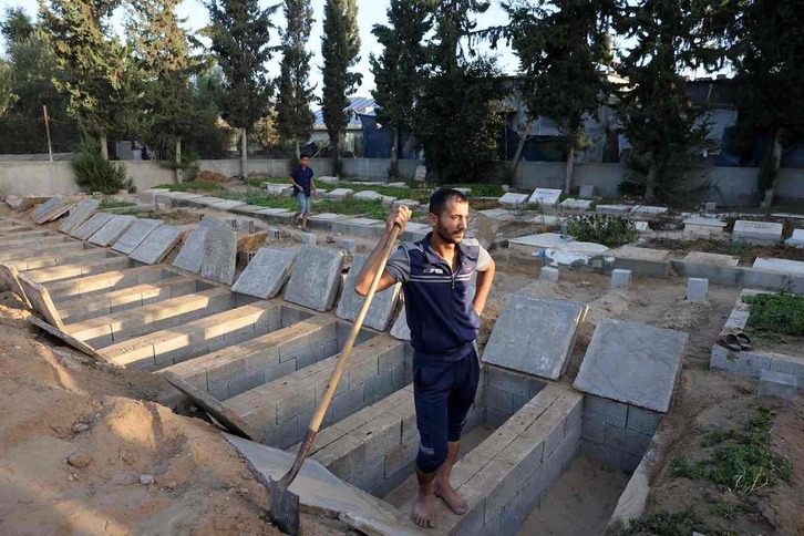Un hombre descansa sobre una hilera de tumbas recién abiertas para la familia Hijazi, en Rafah.