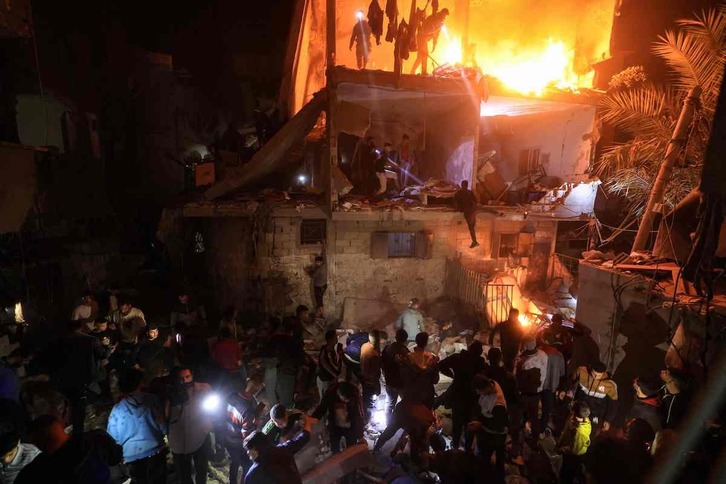 Palestinos buscan supervivientes entre los escombros de un edifico en llamas.