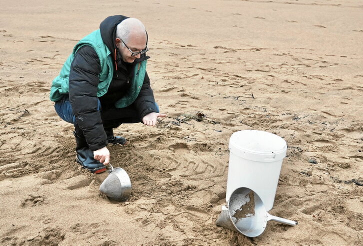 Pertsona bat, plastikozko pinporten laginak jasotzen, Muskizko hondartzan.
