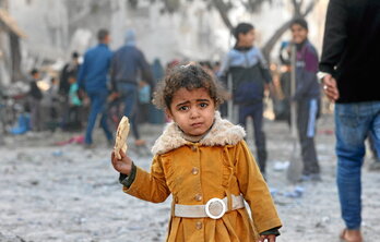Una niña palestina come un trozo de pan mientras se buscan cadáveres entre los escombros tras los bombardeos israelíes en Rafah.