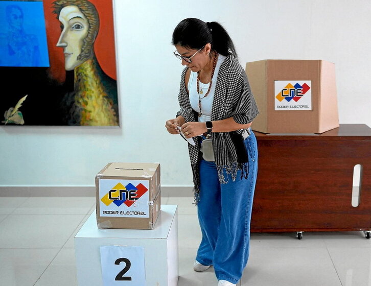 Una electora deposita su voto con un cuadro del libertador Bolívar al fondo.