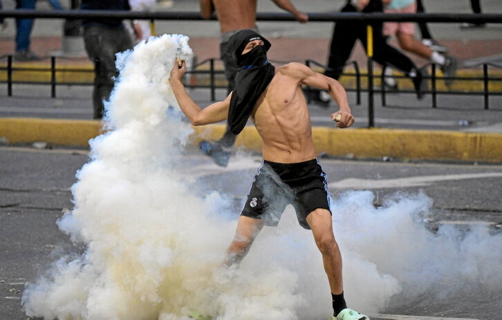 Un opositor venezolano devuelve un bote de humo a los policías en Caracas.