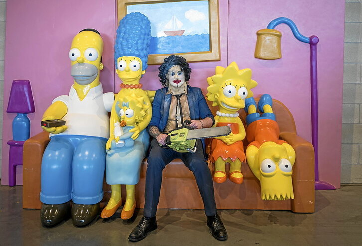 Un hombre disfrazado del personaje Leatherface de “La matanza de Texas” posa para una fotografía en el sofá junto a los muñecos de los miembros de la familia Simpson.