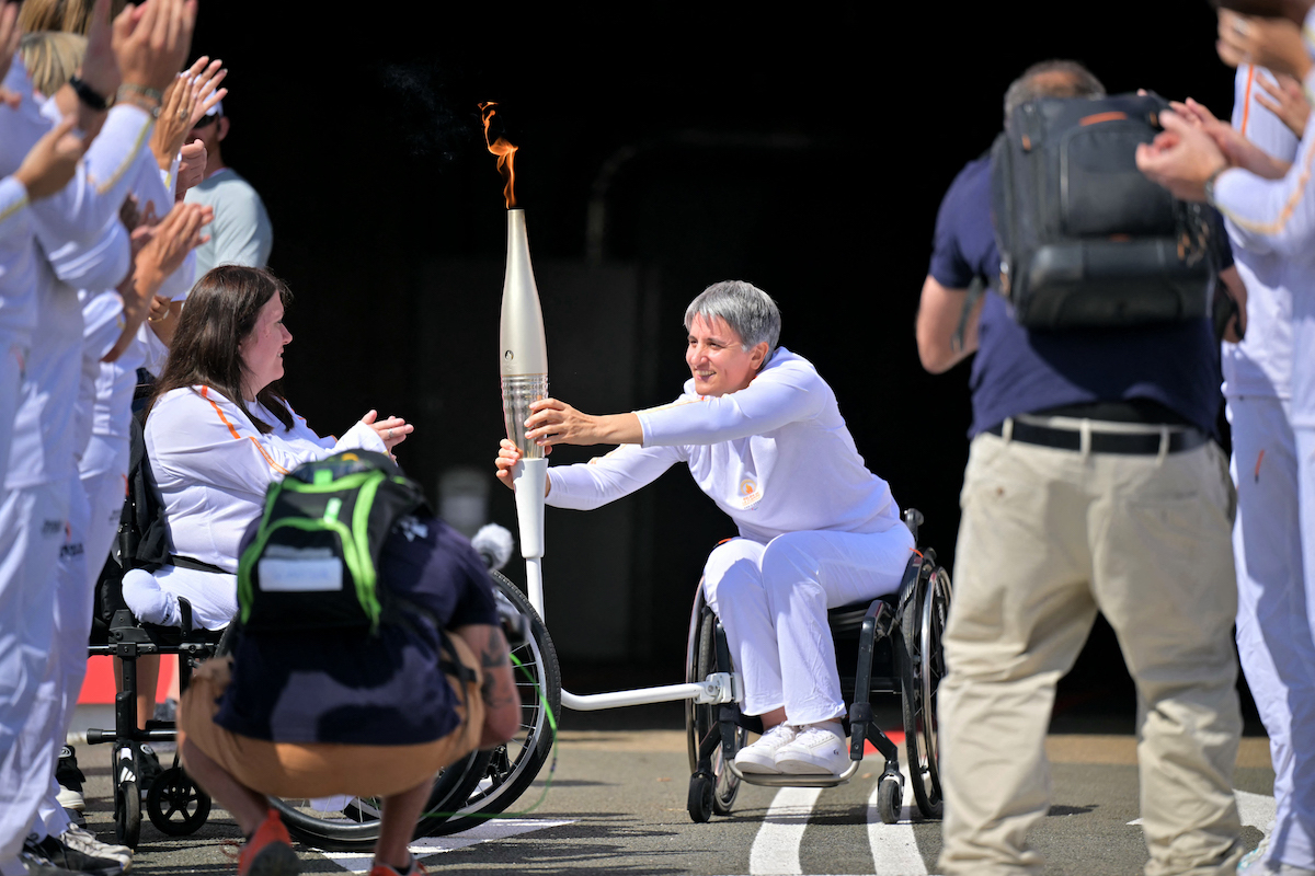 La exdeportista de esgrima en silla de ruedas Emmanuelle Assman porta la antorcha olímpica. (Lou BENOIST/AFP)