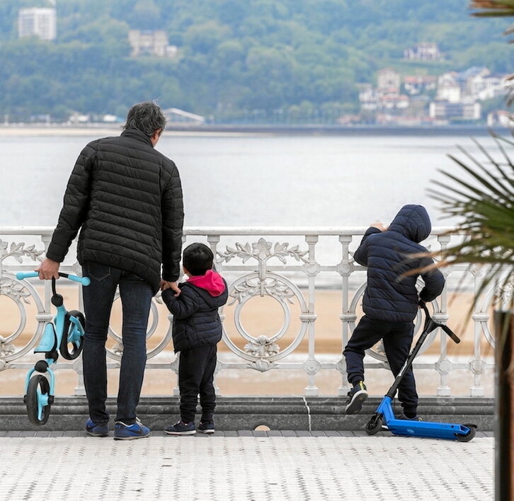 Un padre pasea con sus dos hijos junto a la playa de La Concha.