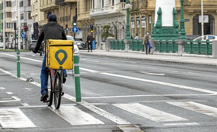 Un repartidor de Glovo atraviesa en bicicleta el puente del Kursaal, en Donostia.
