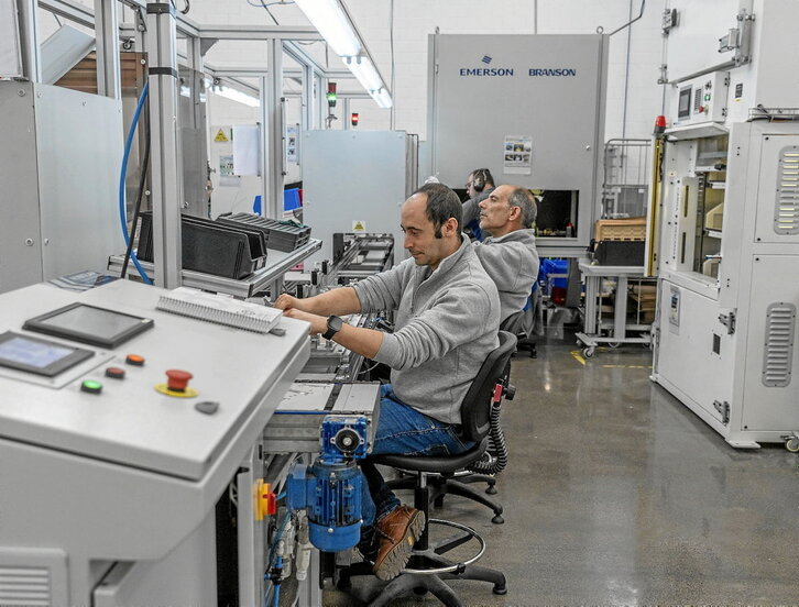 En la página de la izquierda, operarios de Gureak trabajan en una de las líneas de montaje de la división industrial. Sobre estas líneas, instalaciones centrales de Gureak en Goienetxe, en el barrio donostiarra de Berio.