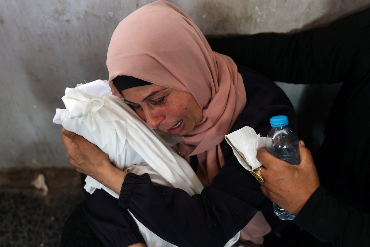 Emakume bat, Israelek erasoan hildako haur baten gorputza eusten. (Omar AL QATAA/AFP)