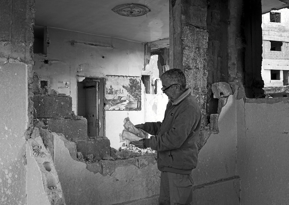 Un hombre lee un libro en una casa derruida.