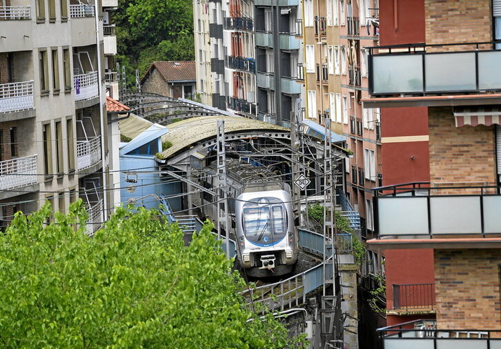 A la izquierda, el Topo atraviesa el pueblo muy cerca de las ventanas de las viviendas. A la derecha, Juan Olalde y Julio Besada, de SOS Antxo, ante la vieja estación que será derribada.