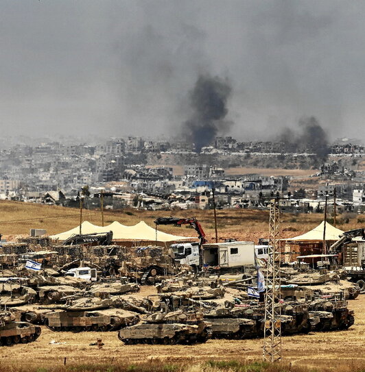 Tanques preparados para la invasión de Gaza, con edificios bombardeados al fondo.