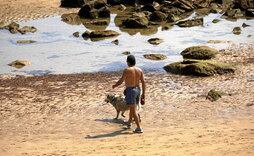 Un hombre pasea con su perro por una playa del litoral vasco.