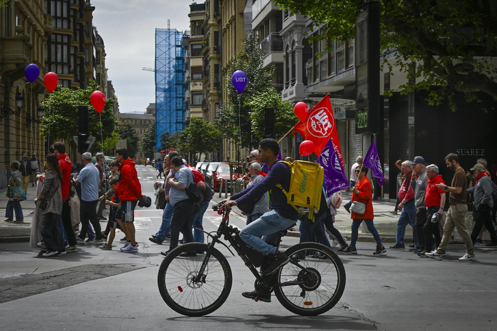 Un repartidor de Glovo pasa junto a la manifestación del Primero de Mayo, en Donostia.