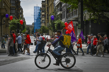 Un repartidor de Glovo pasa junto a la manifestación del Primero de Mayo, en Donostia.