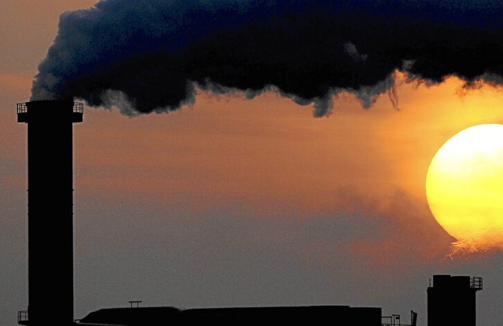 El sol asoma tras el humo vertido por la chimenea de una fábrica en Wismar, Alemania.