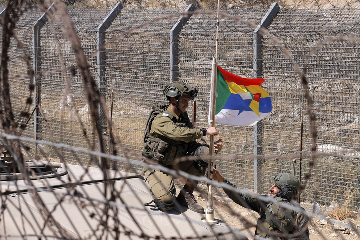 Un militar israelí coloca la bandera drusa en la antena de su tanque