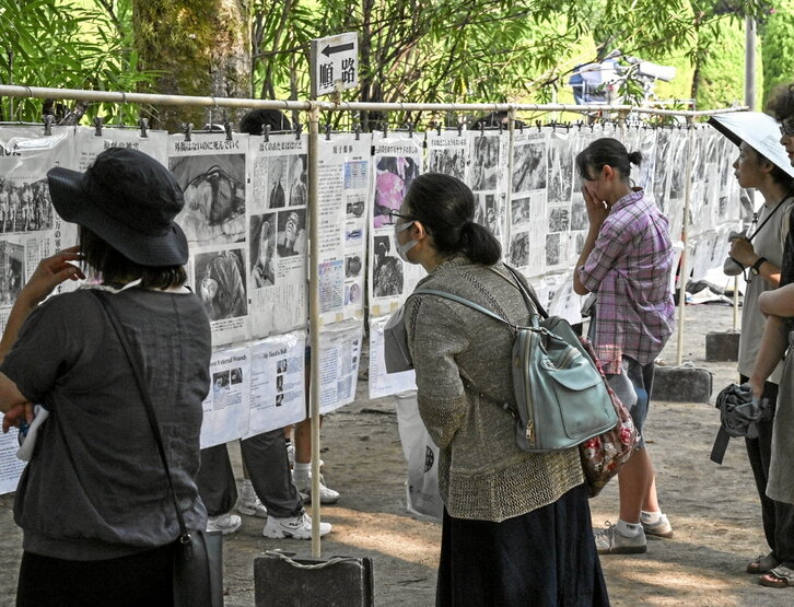 Viandantes leen recortes de periódicos de la época en el Parque Memorial de la Paz.