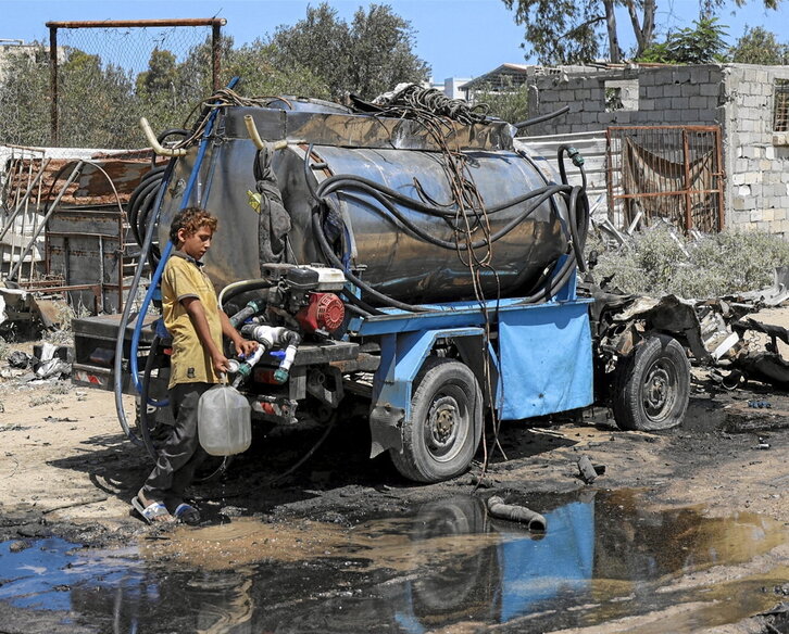 Un niño llena un bidón con el agua del tanque de un camión bombardeado en Nuseirat.