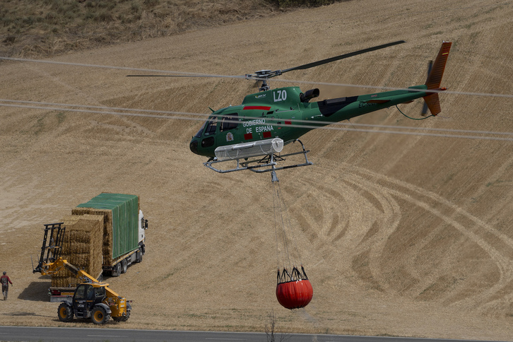 Un helicóptero transporta agua mientras agricultores tratan de salvar sus balas de paja.