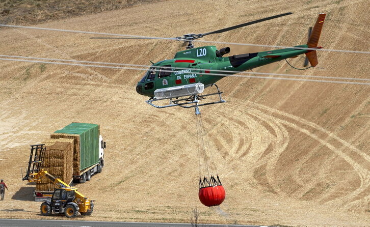 Un helicóptero transporta agua mientras agricultores tratan de salvar sus balas de paja.
