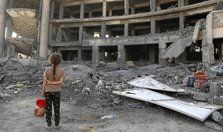 Una niña con un cubo para recoger comida, ante un centro de salud de la Unrwa destruido por Israel en Ciudad de Gaza.