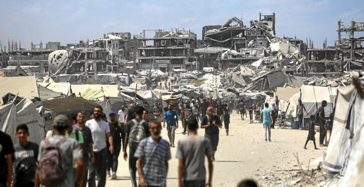 Palestinos caminan por una calle de Ciudad de Gaza, entre tiendas de campaña y edificios destruidos por el Ejército israelí.
