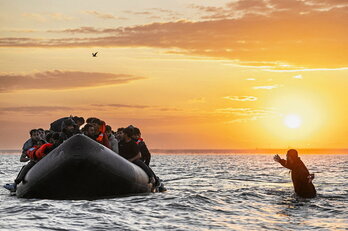 Un migrante corre hacia una lancha en la playa de Gravelines para intentar cruzar el canal de la Mancha hacia Inglaterra.