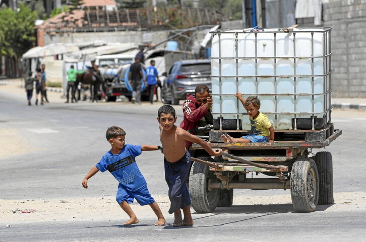 Un hombre y varios niños empujan un carro con un tanque de agua en el campo de regfugiados del Al-Burej (centro).