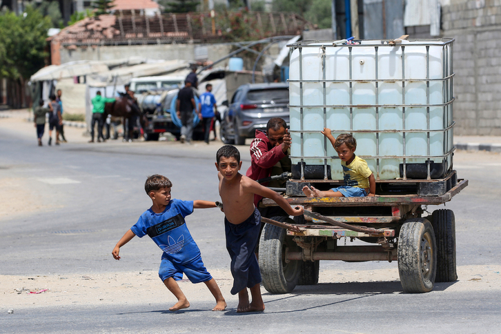 Un hombre y varios niños empujan un carro con un tanque de agua en el campo de regfugiados del Al-Burej.