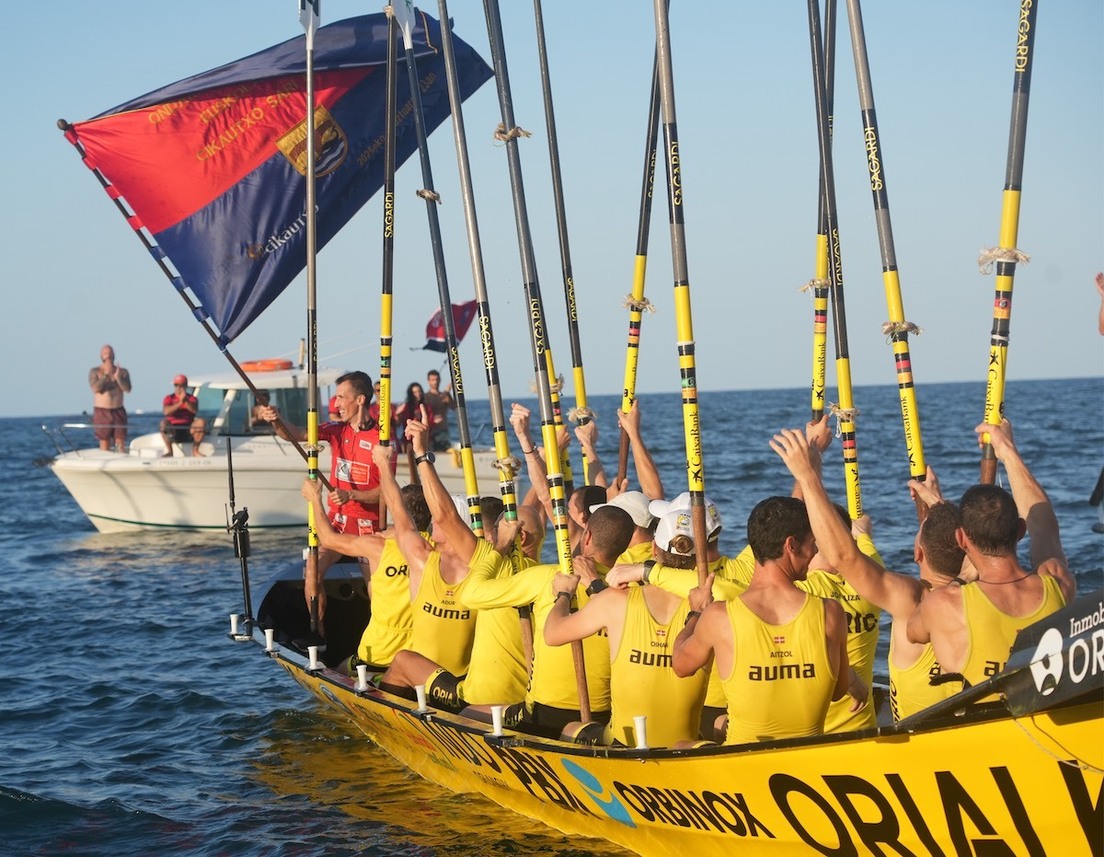Gorka Aranbarri ondea la bandera mientras su tripulación alza los remos.