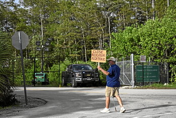 Gizon bat,Alligator Alcatraz ixteko eskatzen duen kartel batekin, etorkinak atxilotzeko zentroaren aurrean astero egiten den erlijioen arteko bijilian.