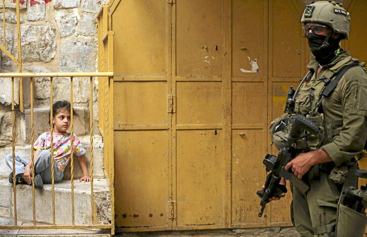 Una niña palestina observa tras unas rejas a un soldado israelí en Hebrón, Cisjordania.