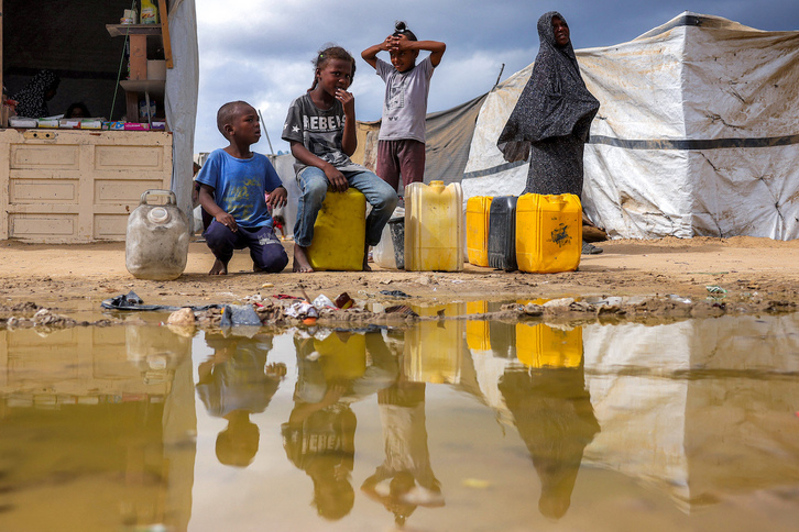 Niños con bidones, junto a un charco en un campamento de desplazados en Deir al-Balah.