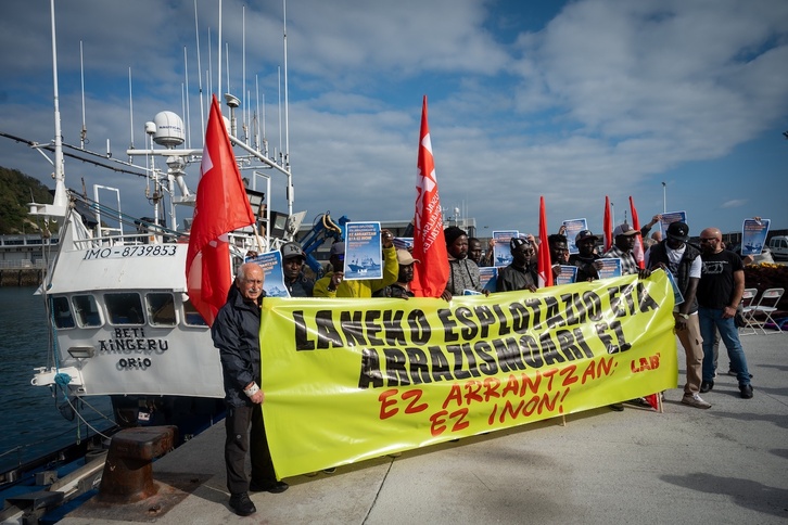 Arrantzales senegaleses y representantes de LAB sujetan una pancarta junto al Beti Aingeru, amarrado en el puerto de Getaria.