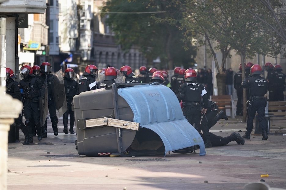 Ertzainas ante un contenedor volcado.